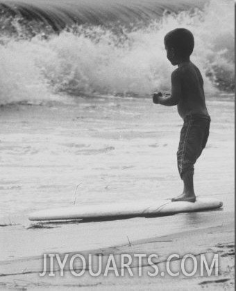 Little Boy Standing on a Surf Board Staring at the Water